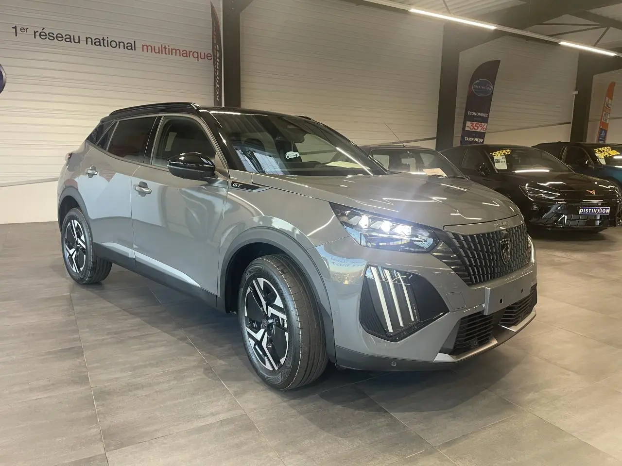 Peugeot 2008 gris en 3/4 avant droit, avec calandre noire et feux LED distinctifs allumés.