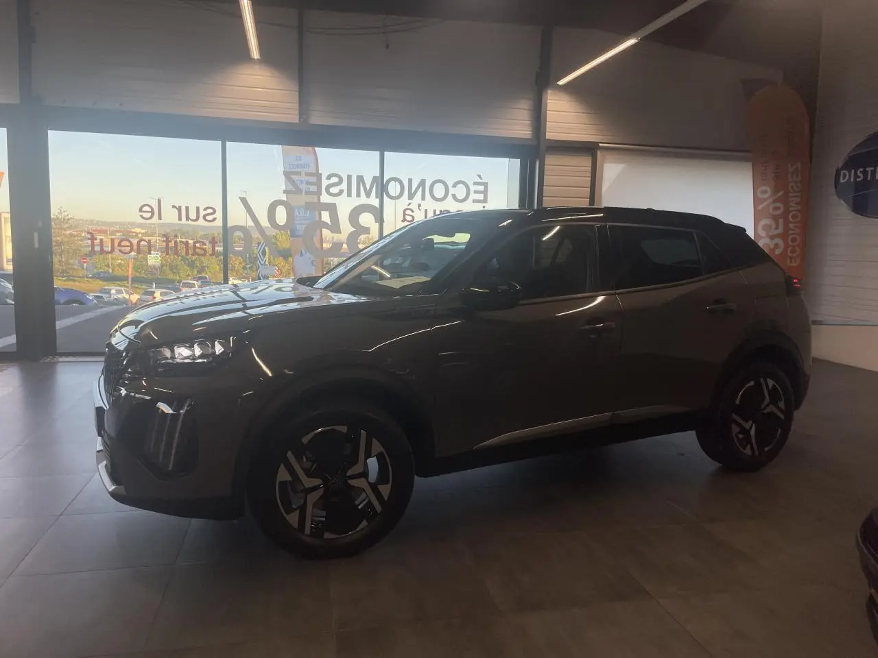 Peugeot 2008 gris en 3/4 avant droit, avec jantes noires et toit contrasté noir en intérieur showroom.