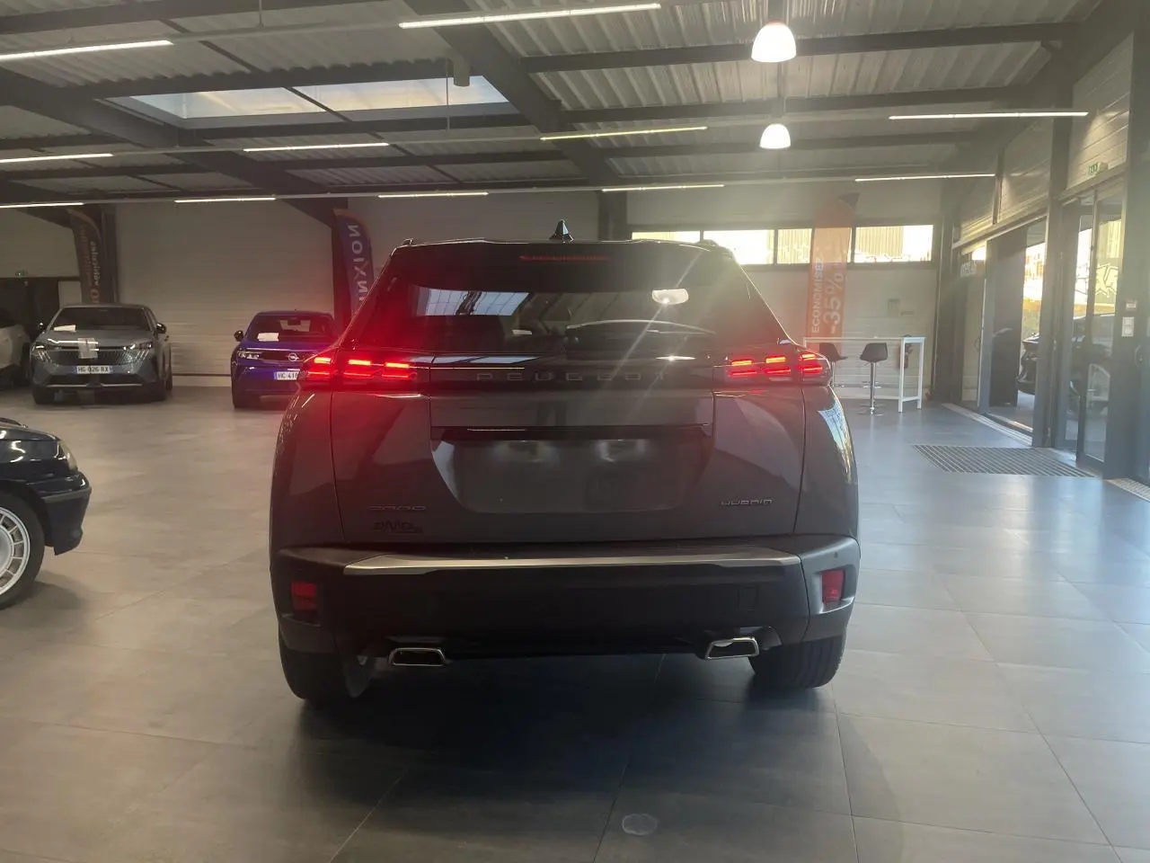 Vue arrière d'un Peugeot 2008 gris métallisé avec feux arrière LED allumés dans un showroom.