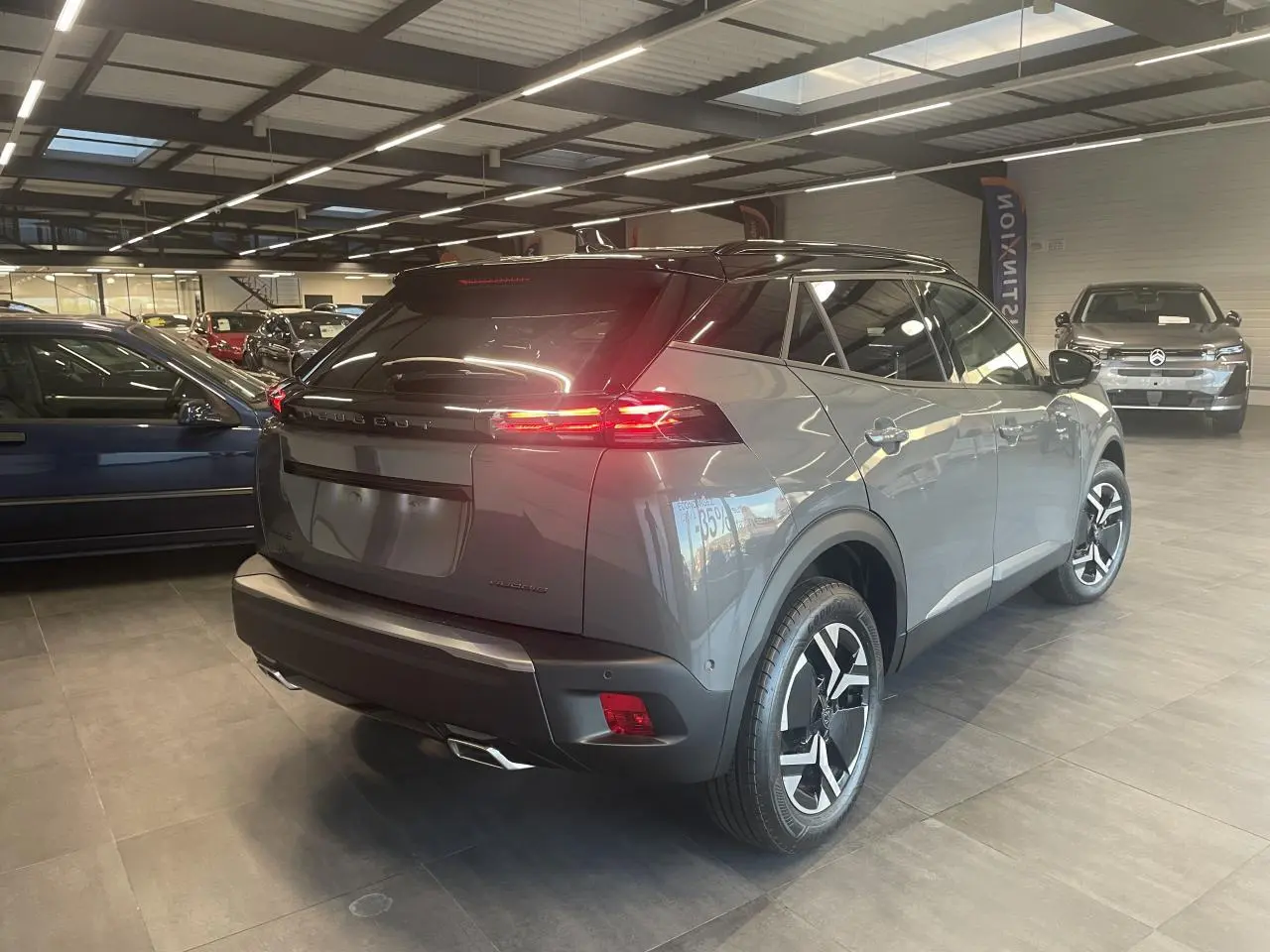 Peugeot 2008 gris métallisé vue 3/4 arrière droit en intérieur avec feux arrière LED allumés.