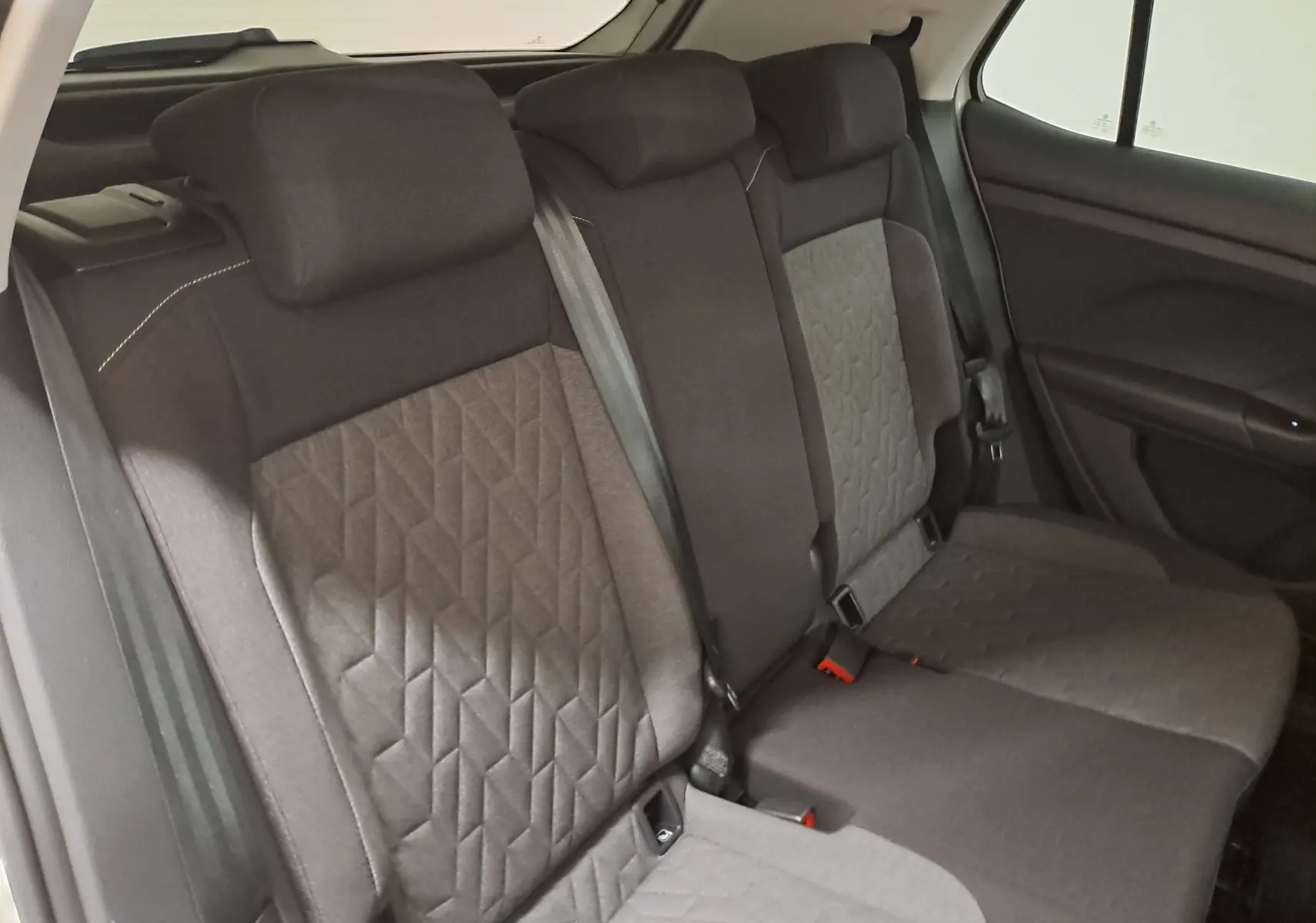 Vue intérieure des sièges arrière du Volkswagen T-Cross 2024, tissu gris avec motifs géométriques et ceintures visibles.