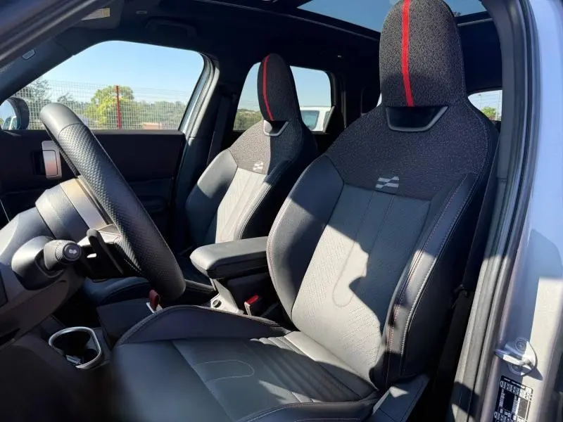 Vue intérieure côté conducteur du MINI Countryman argenté 2025, sièges sport noirs avec bande rouge centrale et volant cuir.