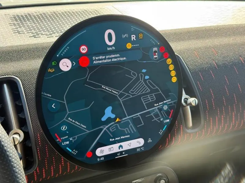 Gros plan sur l'écran tactile circulaire du tableau de bord du MINI Countryman argenté, affichant la navigation et alertes.