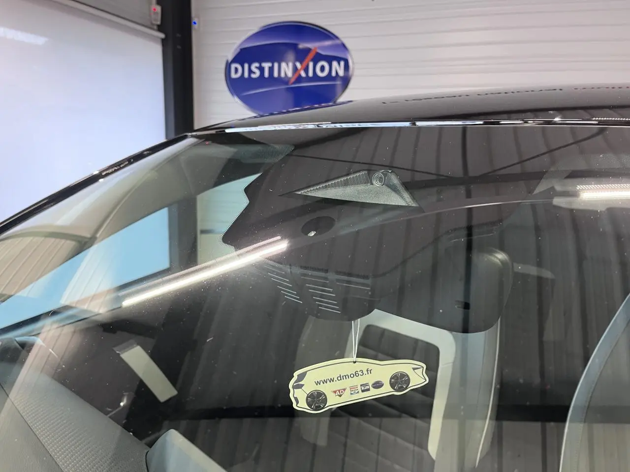 Gros plan sur le pare-brise avant d'une Citroën C4 noire métal, avec caméra et rétroviseur intérieur visibles.