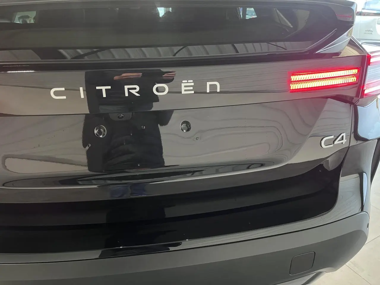 Vue arrière rapprochée de la Citroën C4 noire métallisée avec feux arrière LED allumés et logo distinctif.