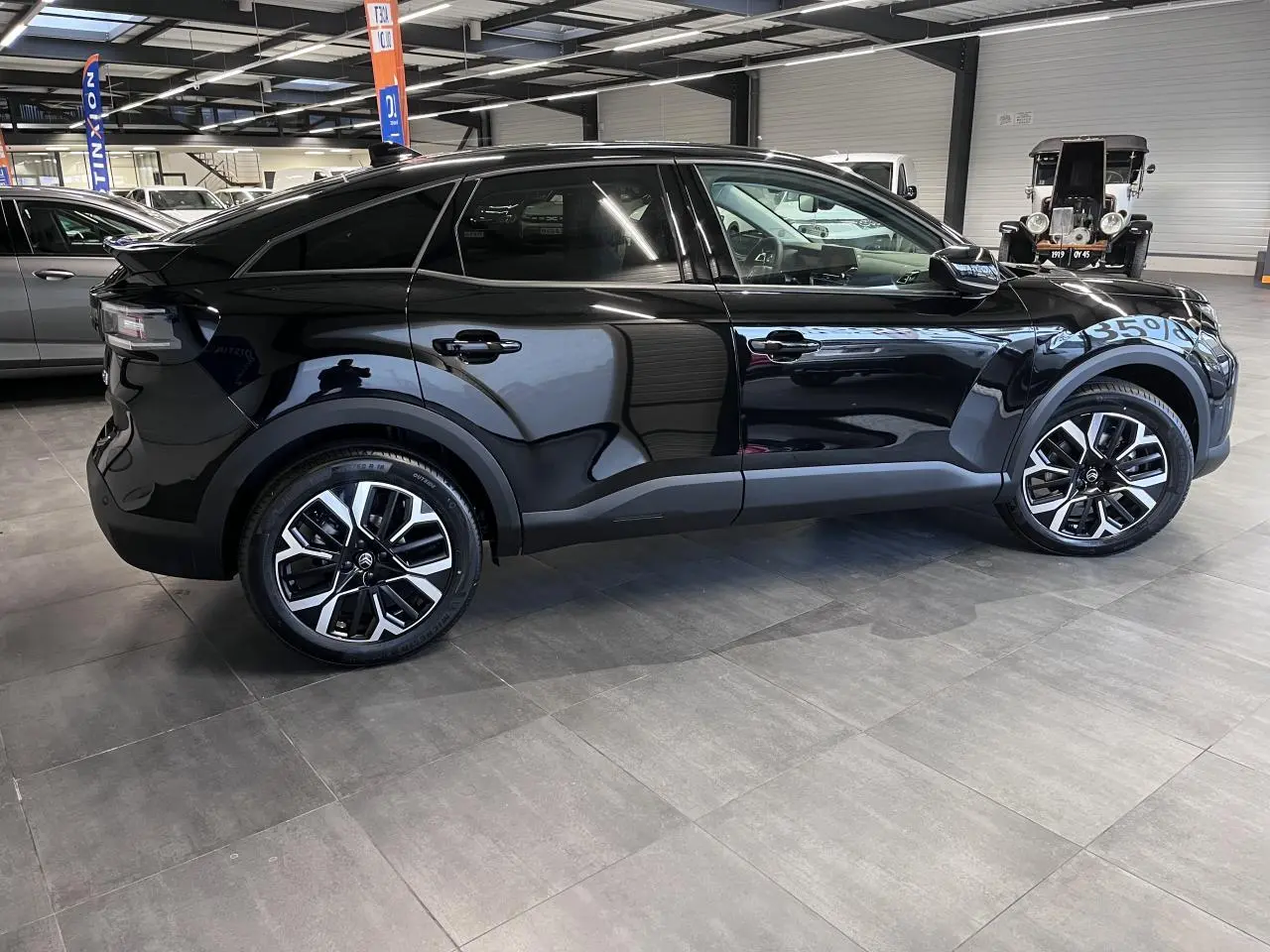 Vue latérale droite d'une Citroën C4 noire métallisée avec jantes alliage 18'' et vitres surteintées en intérieur showroom.