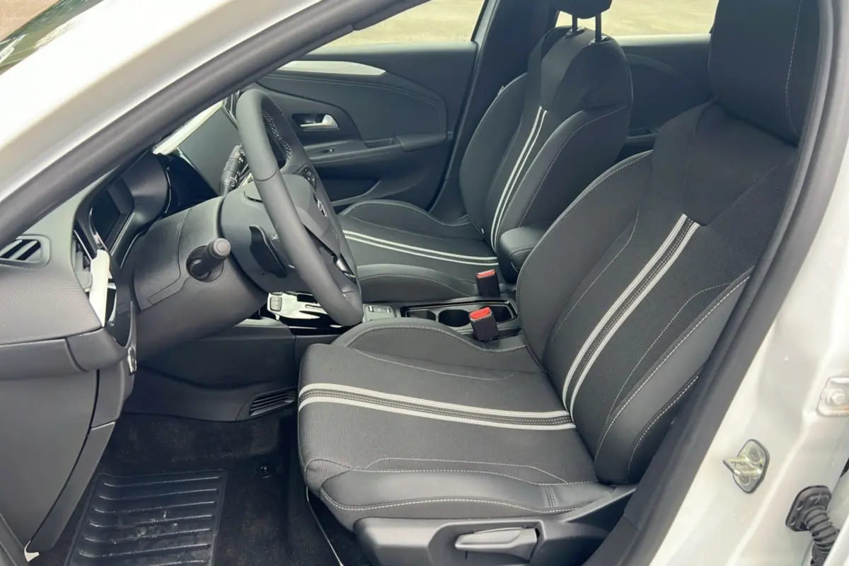 Vue intérieure côté conducteur de l’Opel Corsa blanc kontur, sièges avant noirs avec surpiqûres blanches et volant multifonctions.
