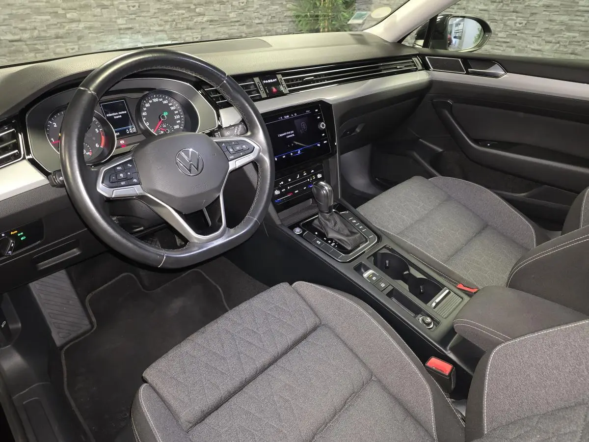 Vue intérieure côté conducteur de la Volkswagen Passat SW 2023, avec tableau de bord noir et sièges tissu gris.