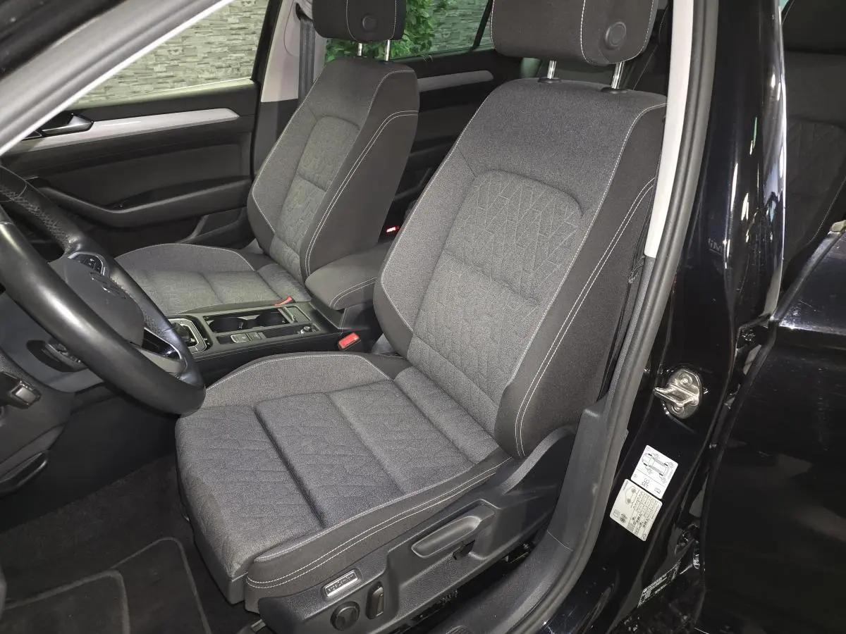 Vue intérieure côté conducteur de la Volkswagen Passat SW 2023 noire, sièges tissu gris avec surpiqûres blanches.
