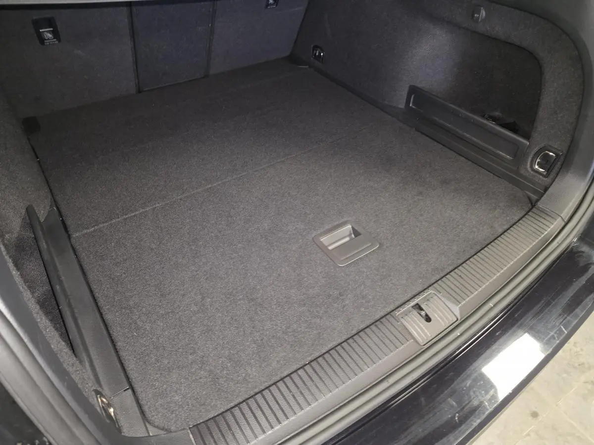 Coffre spacieux de Volkswagen Passat SW noir vu de dessus, avec tapis de sol et anneaux d'arrimage visibles.