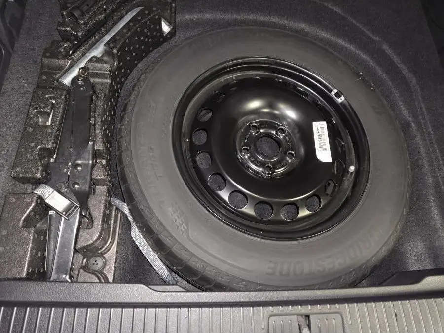 Vue rapprochée de la roue de secours noire en acier dans le coffre d'une Volkswagen Passat SW 2023, avec cric adjacent.