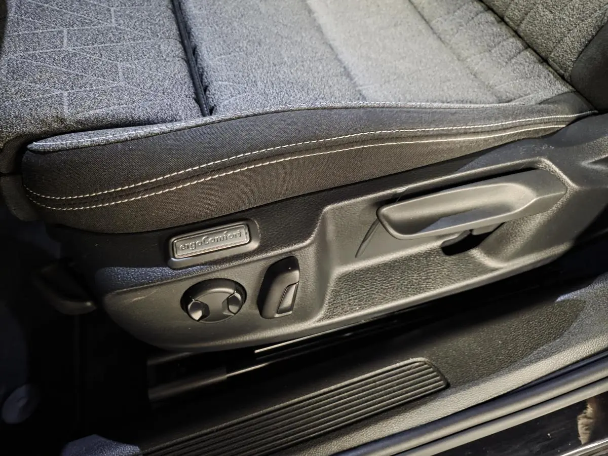 Gros plan sur la commande de réglage du siège avant tissu noir avec surpiqûres blanches de la Volkswagen Passat SW 2023.