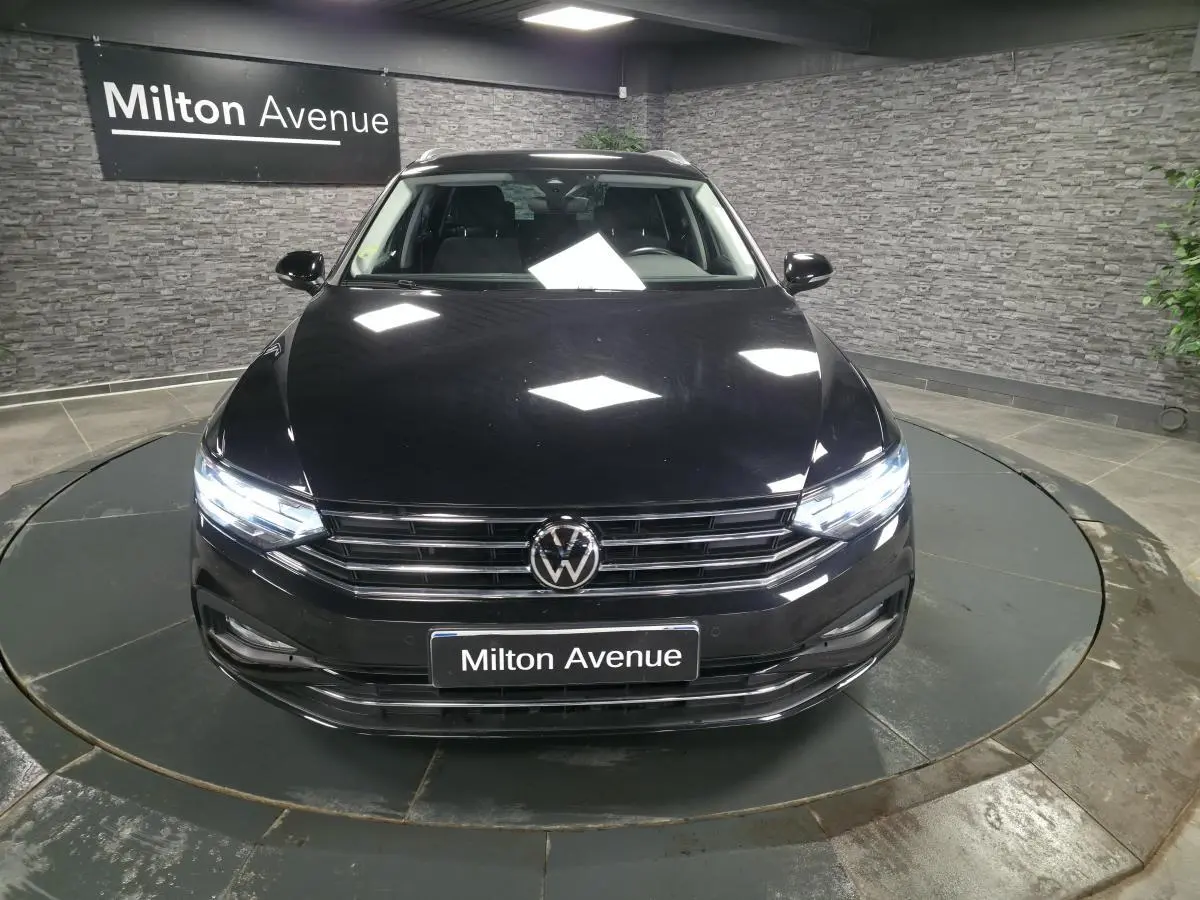 Vue avant d'une Volkswagen Passat SW noire avec phares allumés dans un showroom au sol gris.