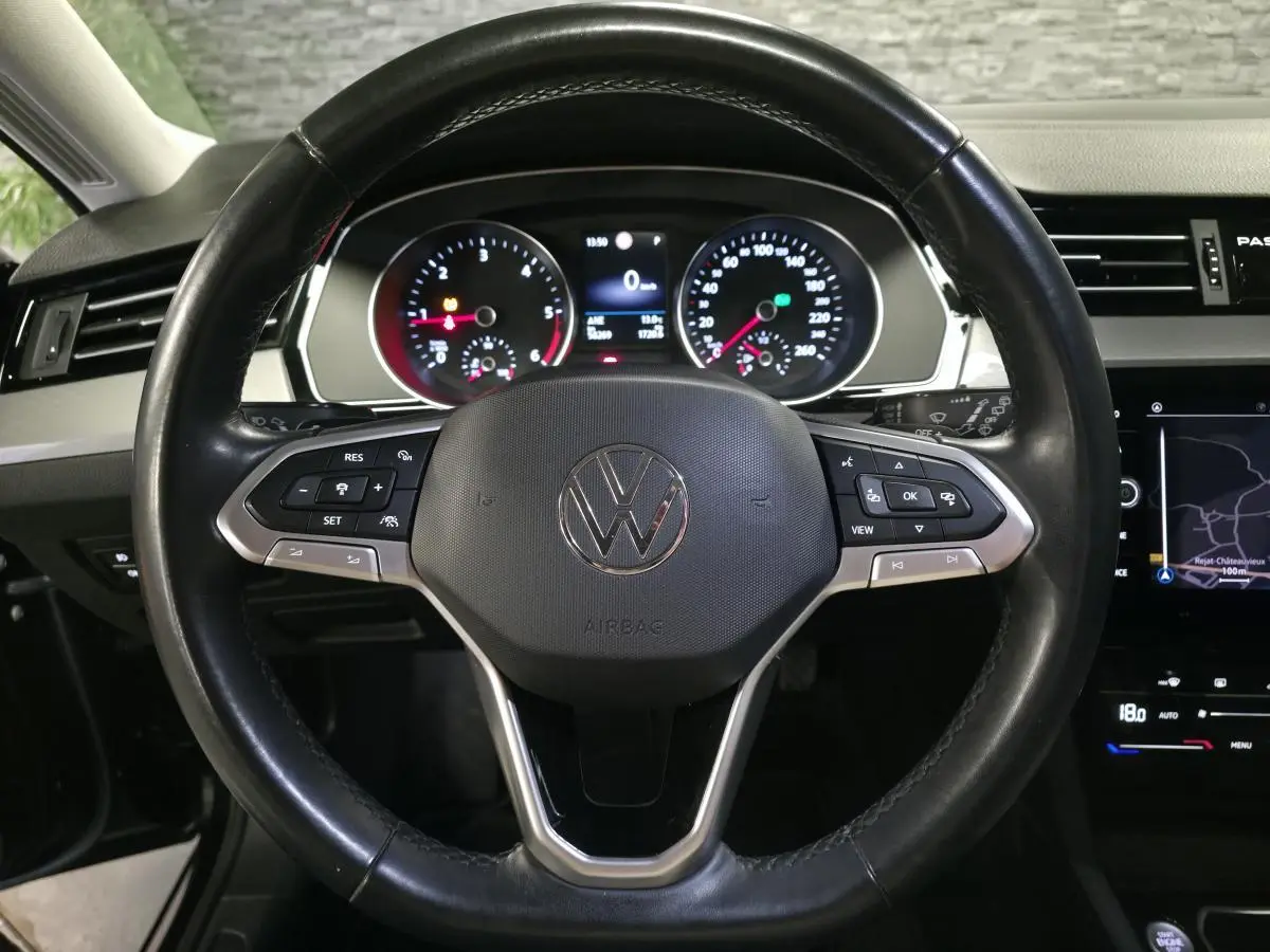 Vue intérieure centrée sur le volant cuir multifonction noir de la Volkswagen Passat avec tableau de bord et écran tactile visibles.