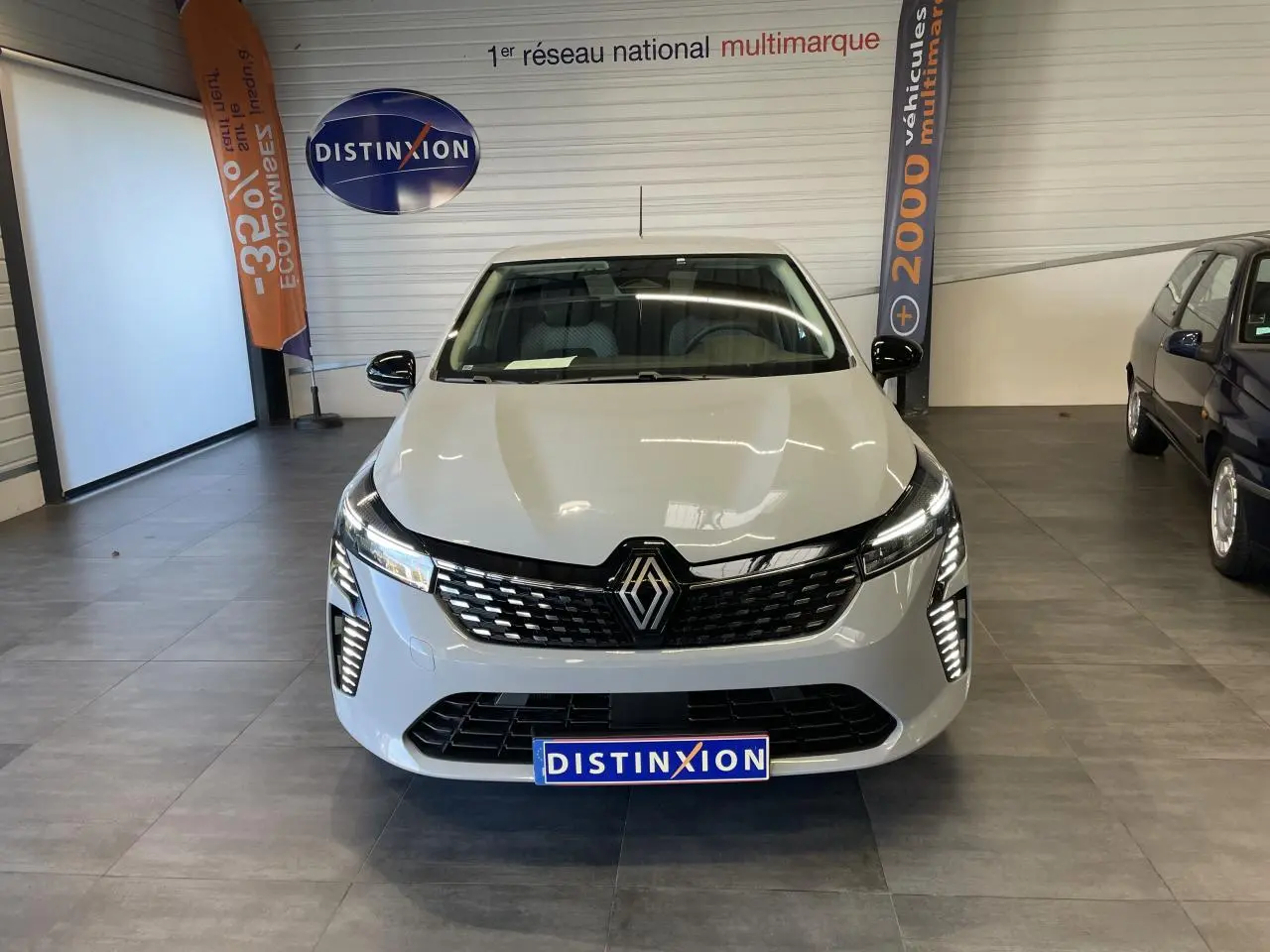 Vue avant d'une Renault Clio 2025 gris Rafale avec calandre noire et feux LED allumés en showroom.