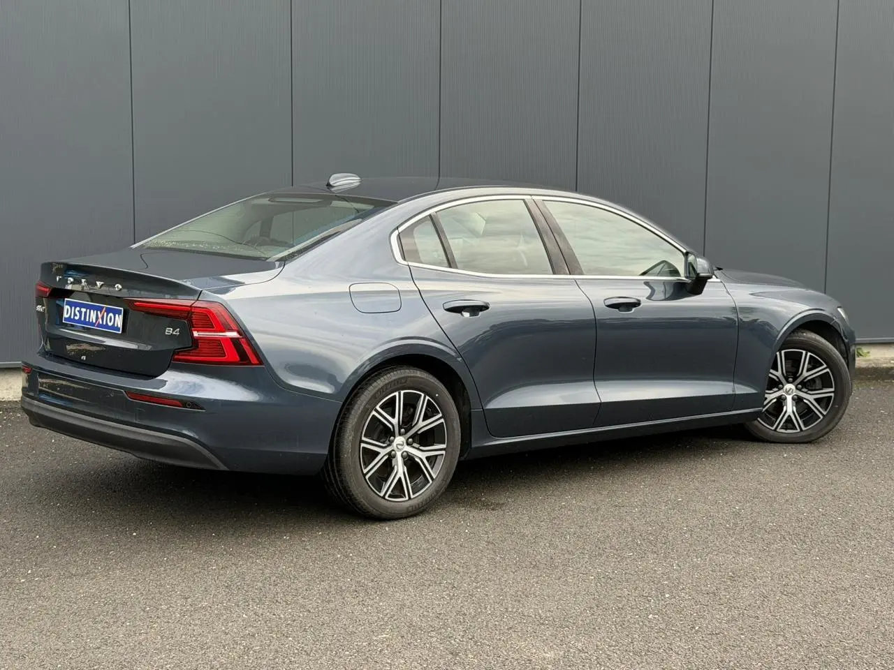 Vue 3/4 arrière côté droit d'une Volvo S60 B4 197 DCT7 MHEV Core+ gris Denim avec jantes alliage 17 pouces.