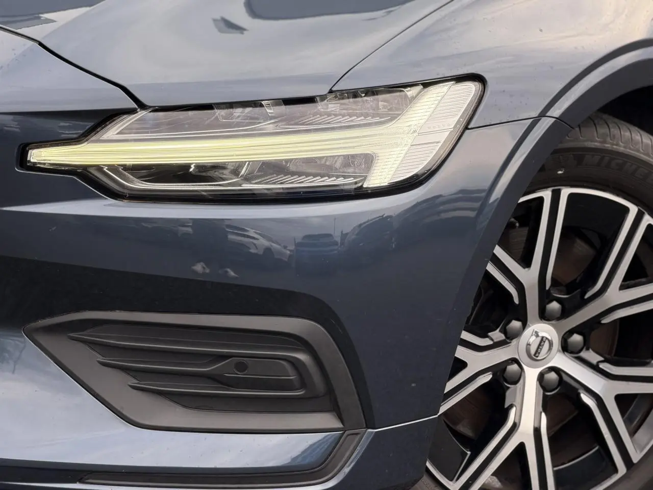 Gros plan sur l'avant droit gris Denim du Volvo S60 2024, mettant en valeur le phare LED et la jante alliage 17 pouces.
