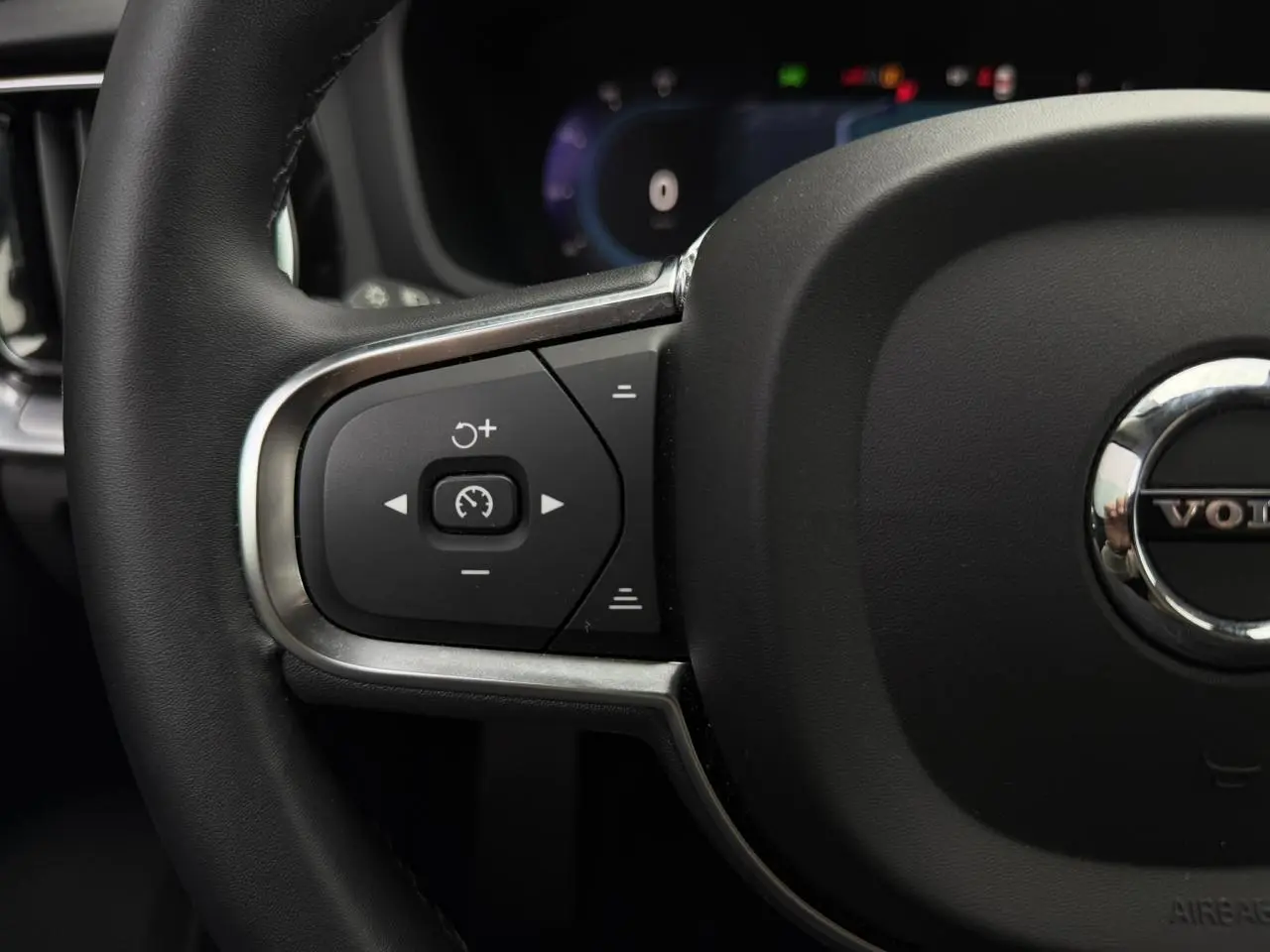 Gros plan sur le volant noir de la Volvo S60 2024 avec commandes intégrées et logo central chromé.