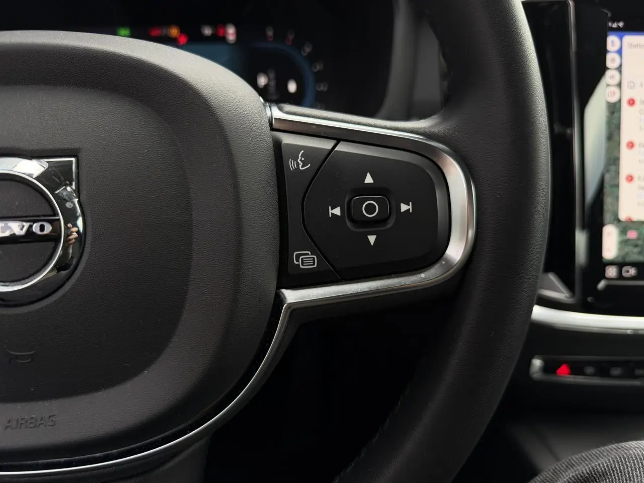 Gros plan sur le côté droit du volant noir de la Volvo S60 2024 avec commandes vocales et multimédia visibles.