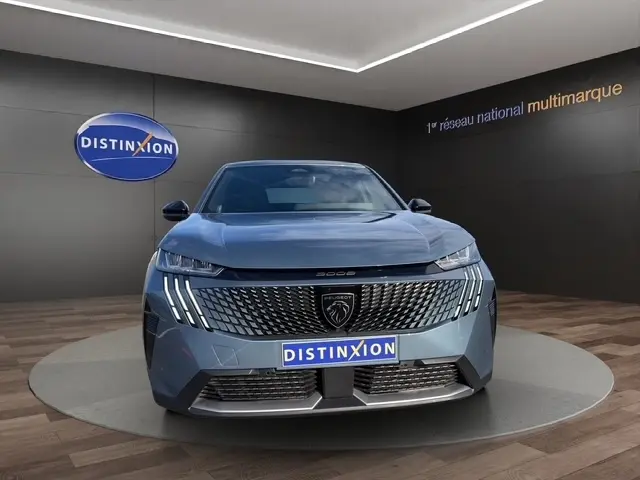Vue avant d'un Peugeot 3008 bleu 2026 avec calandre distinctive et feux LED verticaux allumés dans un showroom.