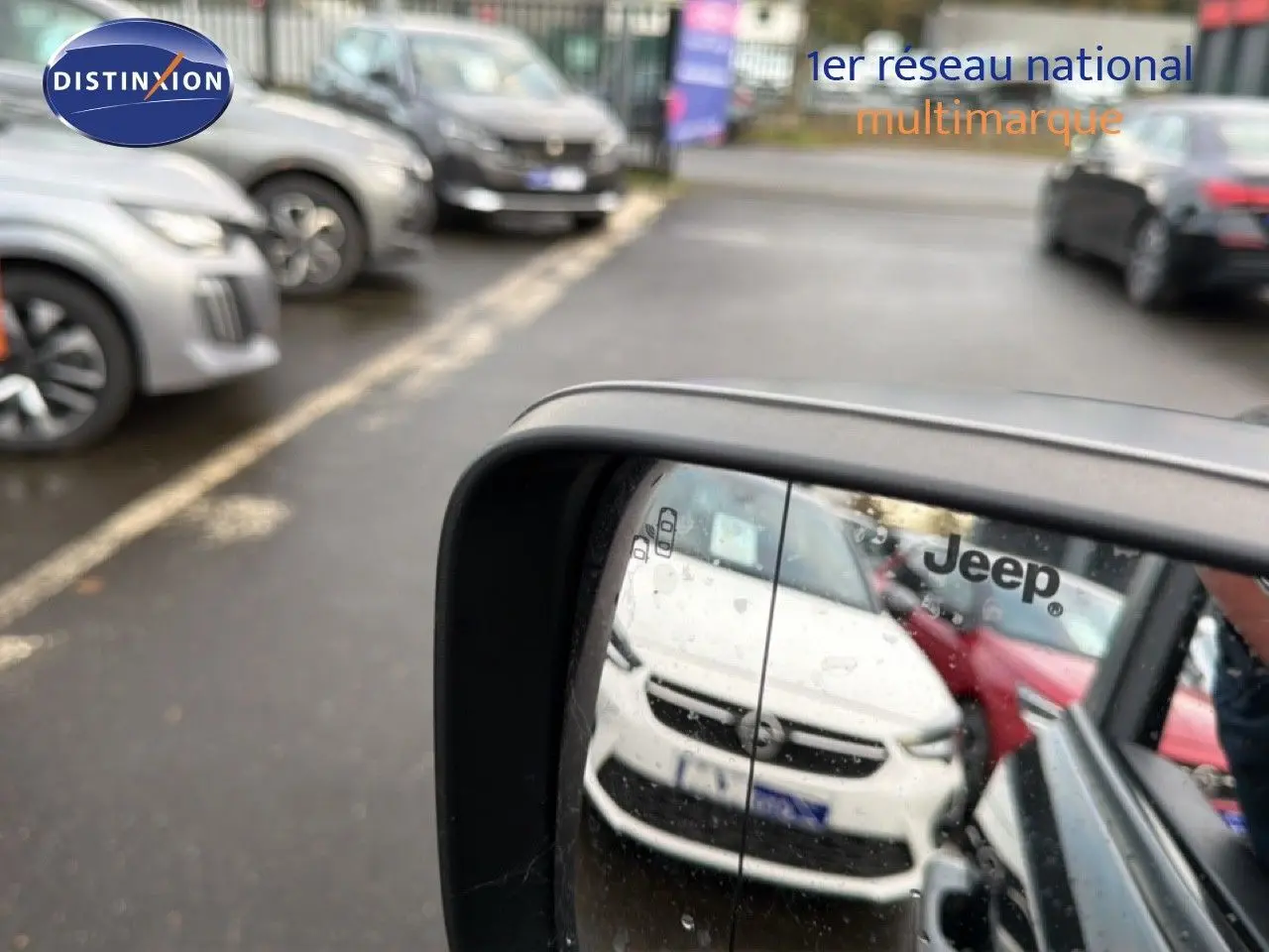 Rétroviseur latéral droit montrant la face avant blanche d'un Jeep Renegade en stationnement.