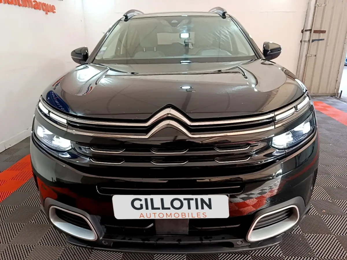 Vue de face d'un Citroën C5 Aircross Hybrid 225 ë-EAT8 Shine noir avec phares LED allumés dans un showroom.