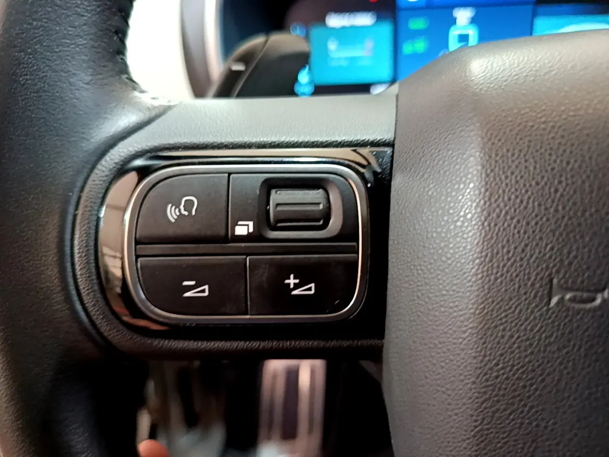 Gros plan sur les commandes gauche du volant cuir du Citroën C5 Aircross Hybrid noir, avec affichage digital en arrière-plan.