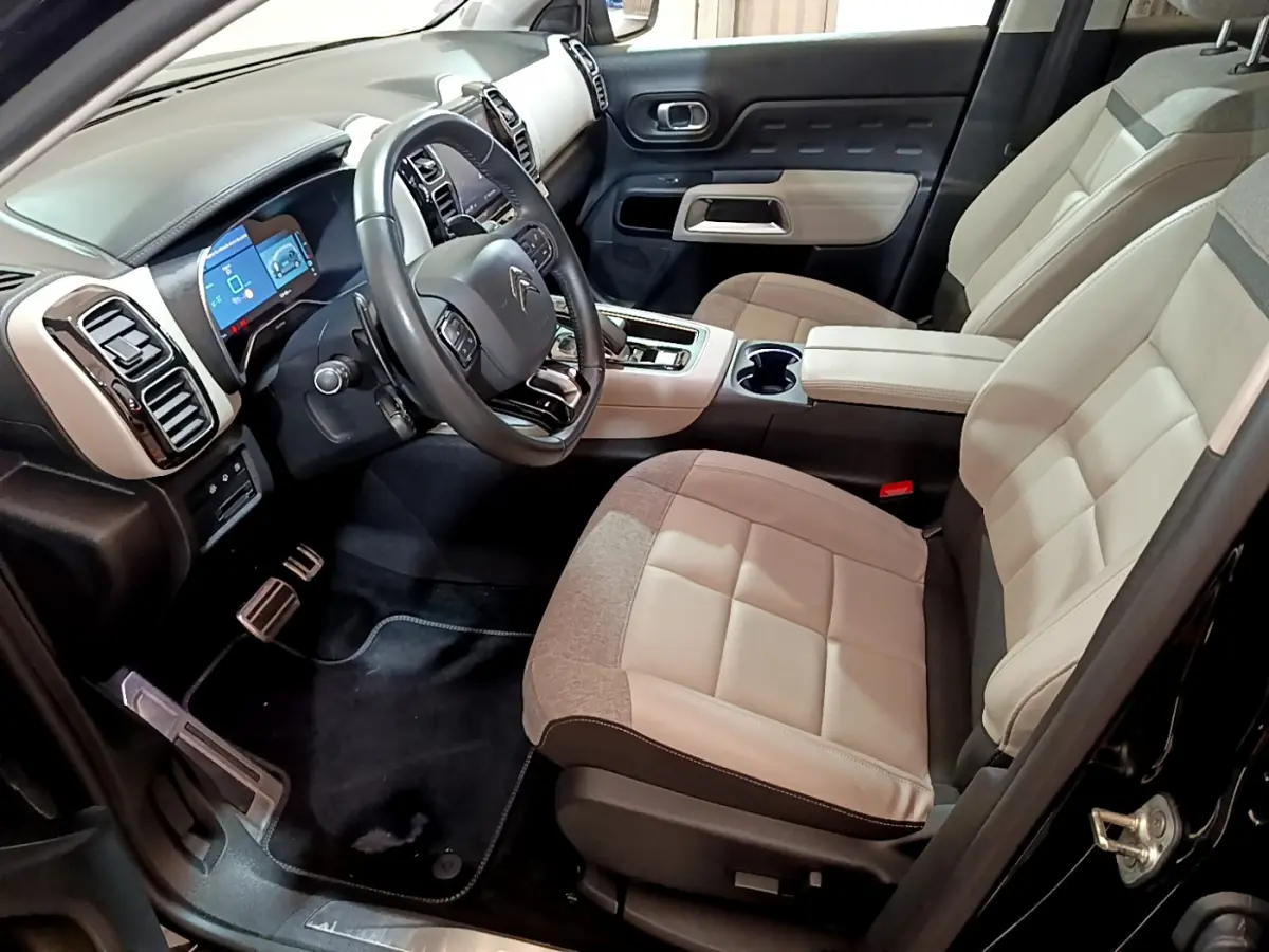 Intérieur clair du Citroën C5 Aircross Hybrid 225, vue côté conducteur avec tableau de bord et sièges beige et gris.