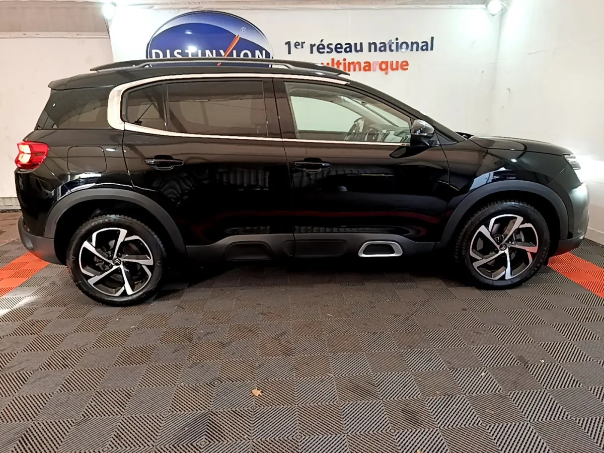 Profil côté droit d'un Citroën C5 Aircross Hybrid 225 noir, avec jantes alliage et barres de toit chromées visibles.