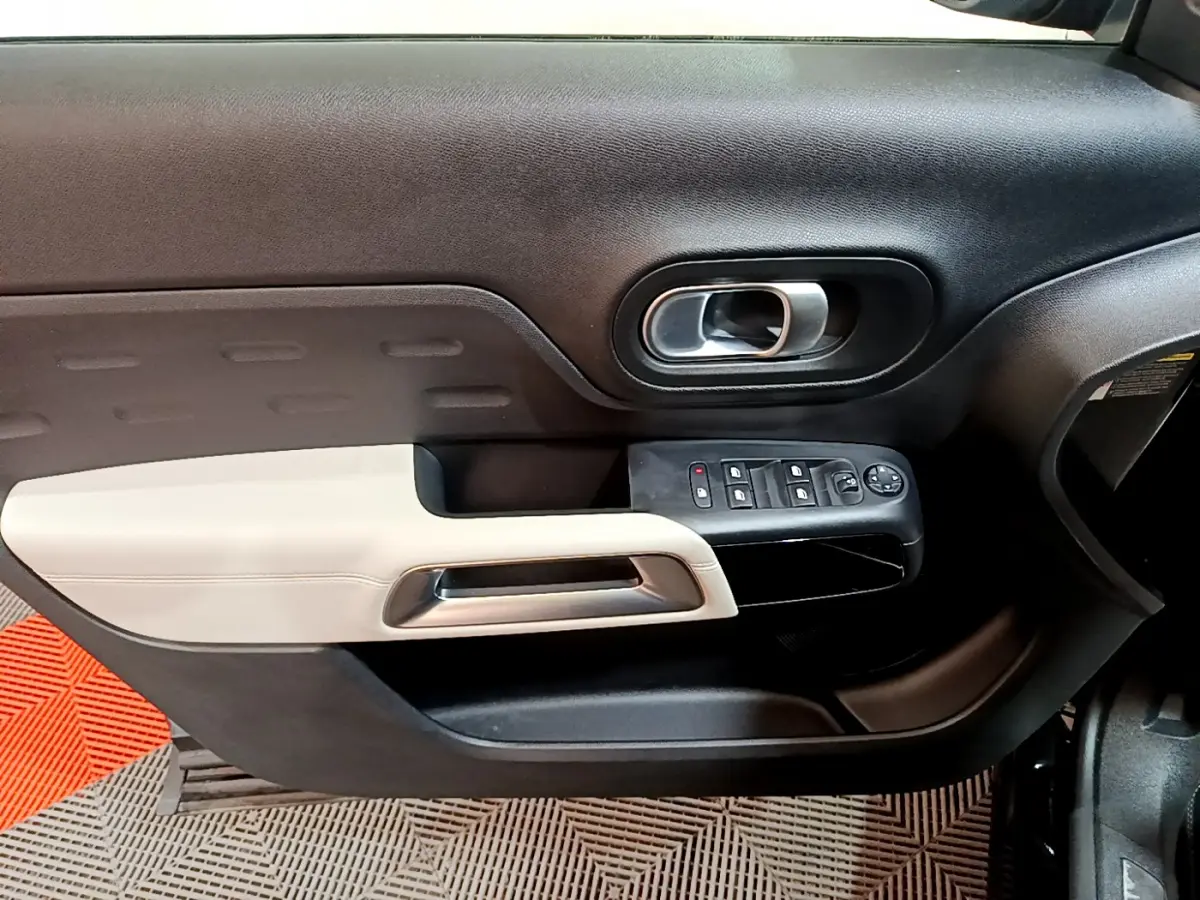 Intérieur côté gauche de la porte avant noire et beige du Citroën C5 Aircross Hybrid 225 ë-EAT8 Shine, avec commandes électriques.