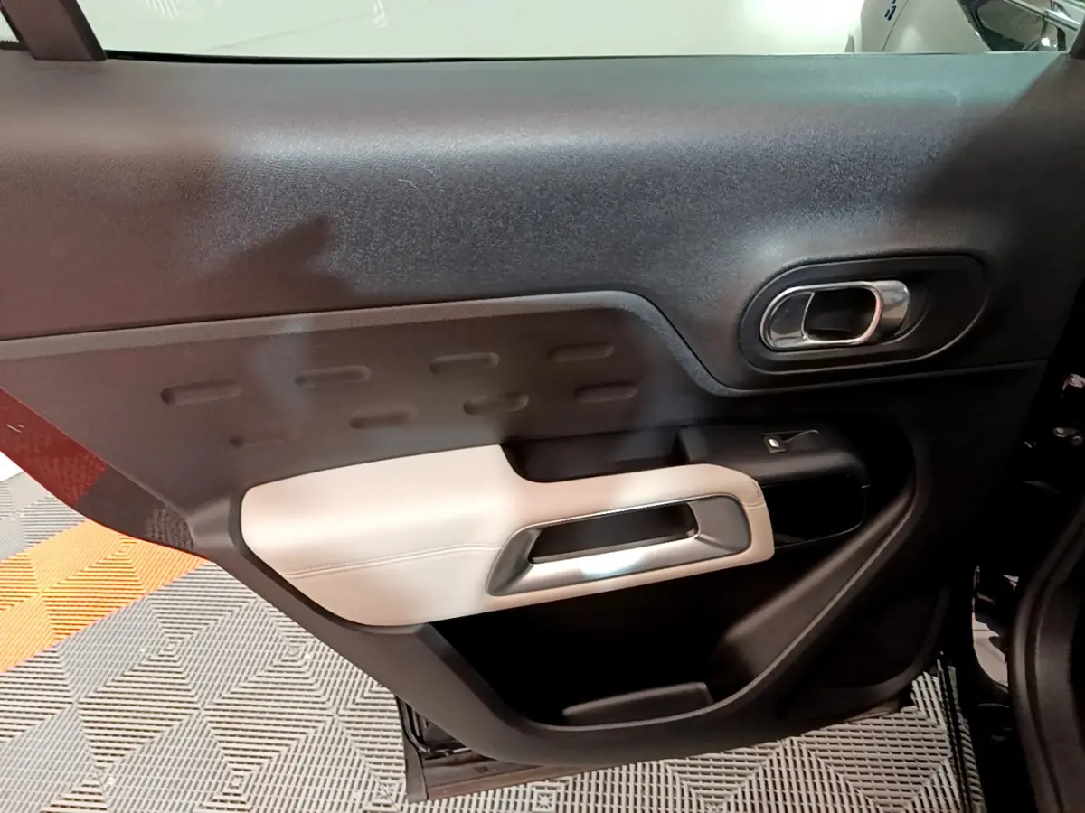 Gros plan sur la garniture intérieure de la porte côté gauche du Citroën C5 Aircross Hybrid noir, avec accoudoir clair et poignée chromée.