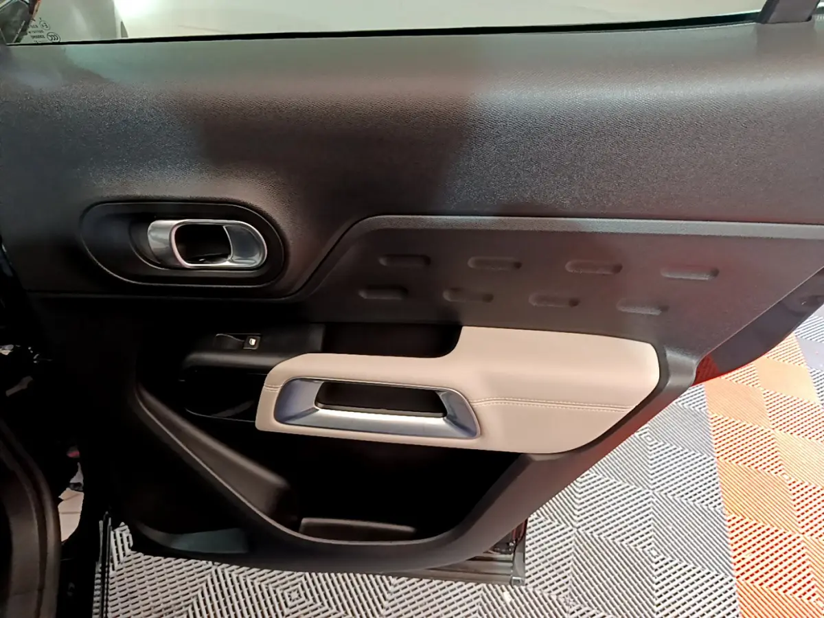 Vue intérieure du panneau de porte côté gauche du Citroën C5 Aircross Hybrid noir, avec insert beige et poignée argentée.