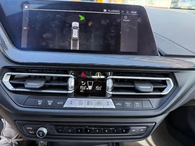 Vue rapprochée du tableau de bord de la BMW Série 1 gris foncé, avec écran tactile et commandes climatisation visibles.