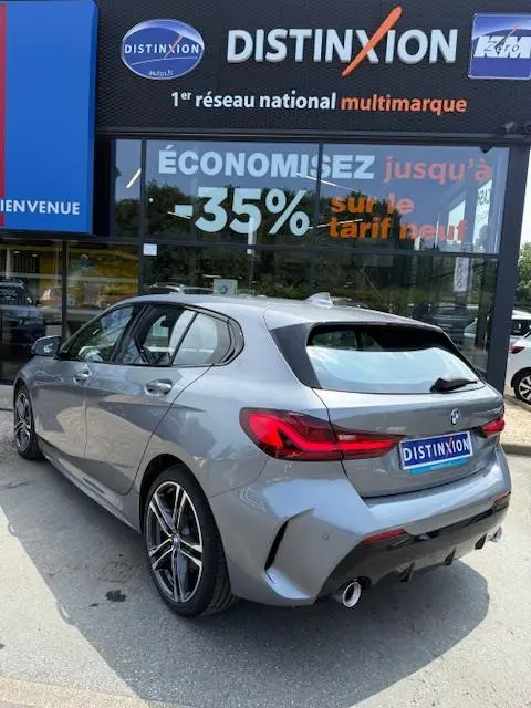 BMW Série 1 118d Edition Sport gris foncé vue 3/4 arrière droit devant un showroom Distinxion.
