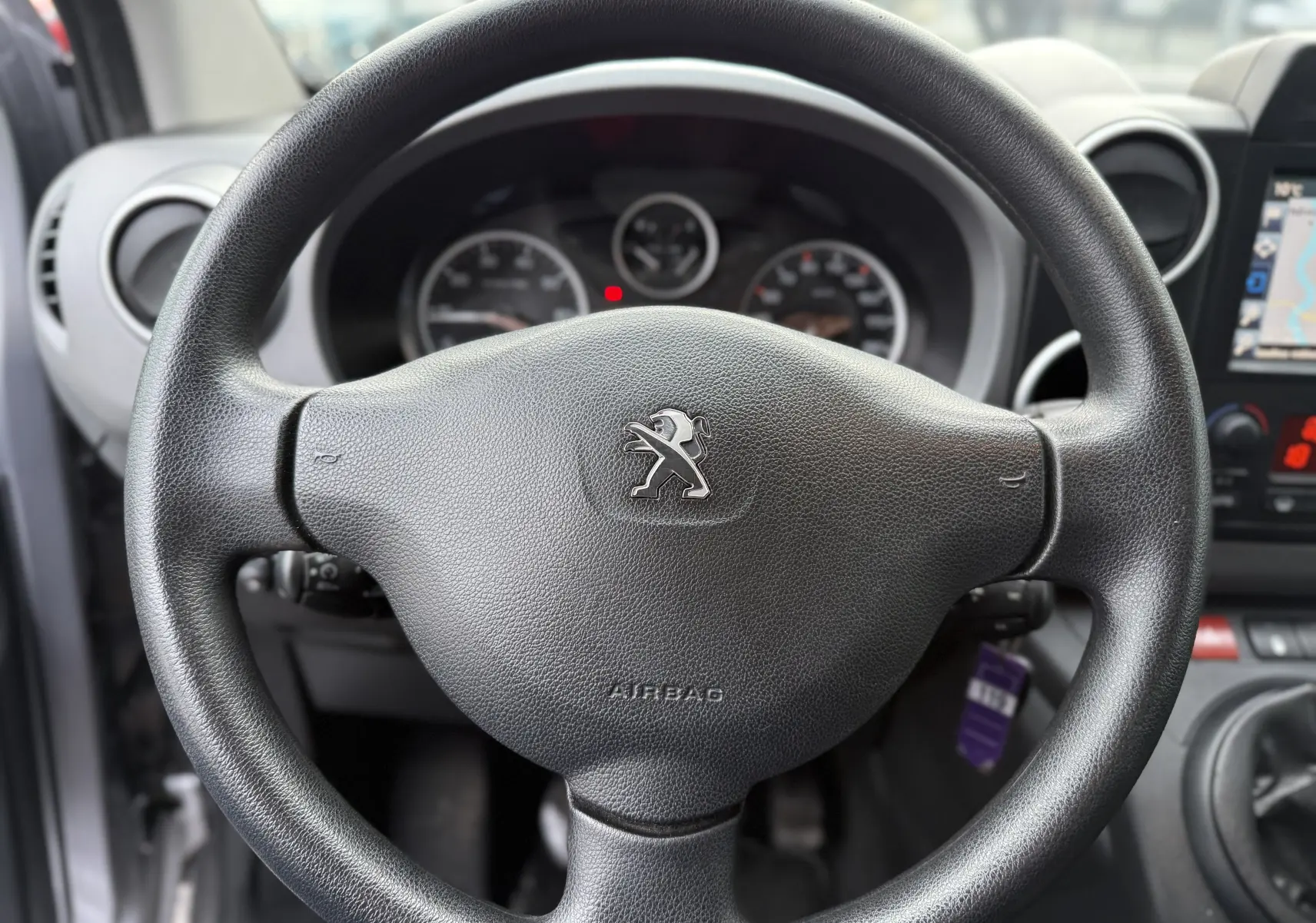 Vue rapprochée du volant noir de la Peugeot Partner Tepee 2018 avec tableau de bord et écran GPS partiellement visibles.