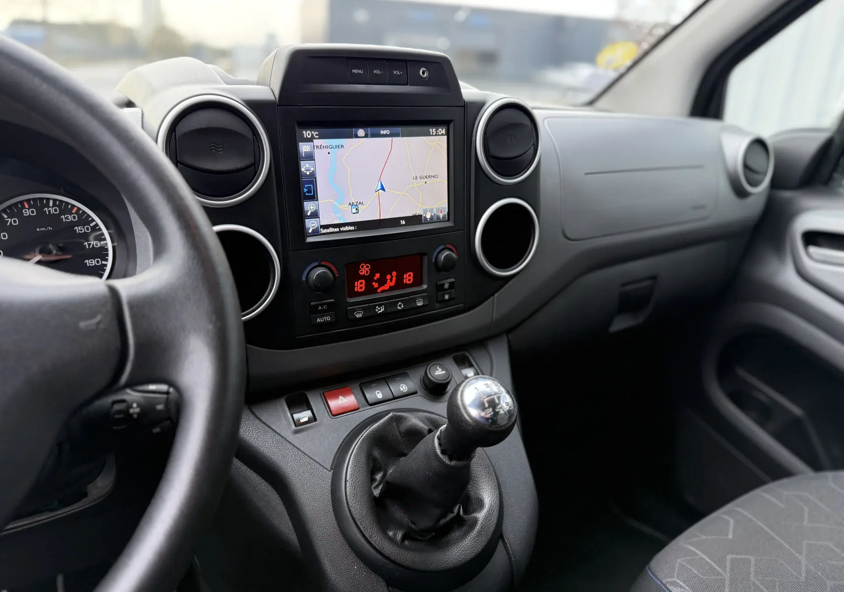 Vue intérieure centrée sur la console centrale et levier de vitesses manuelle du Peugeot Partner Tepee gris avec écran GPS et commandes climatisation.