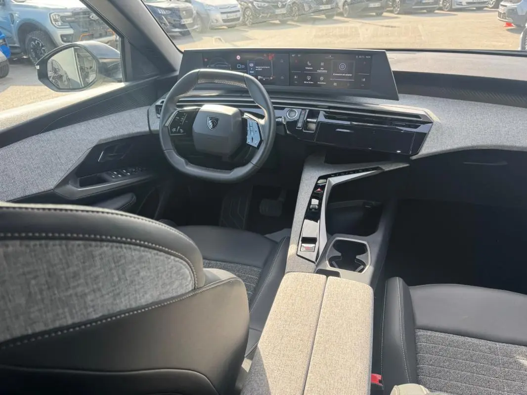 Vue intérieure avant du Peugeot 3008 Hybrid 145 Allure 2025 noir, avec cockpit numérique et sellerie tissu gris.