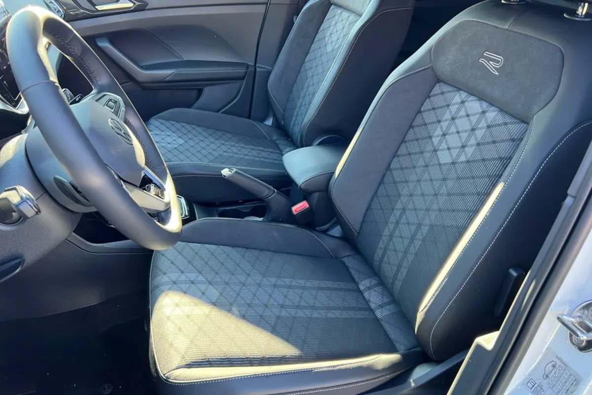 Vue intérieure côté conducteur du Volkswagen T-Cross TSI 116 DSG7 R-Line 2025, sièges tissu noir avec logo R brodé.