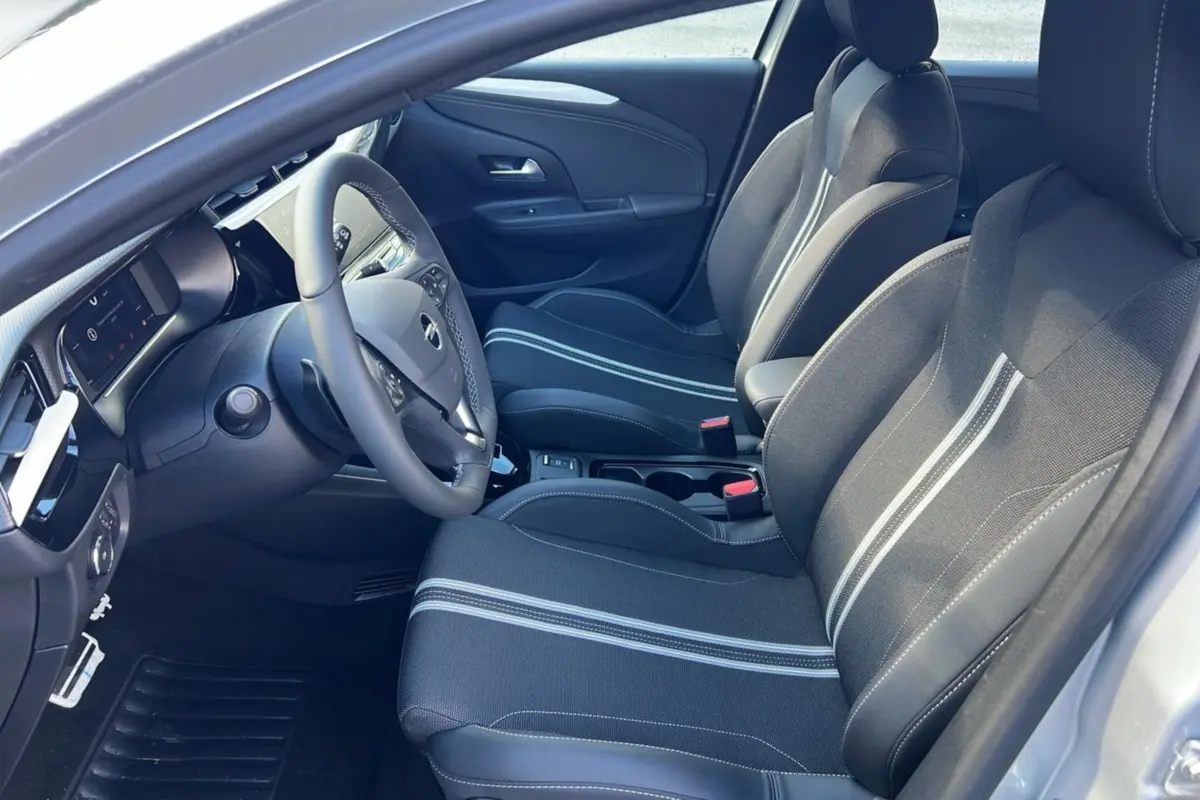 Vue intérieure côté conducteur de l’Opel Corsa Hybrid 110 e-DCT6 gris kristall, sièges tissu avec bandes claires et volant cuir multifonctions.