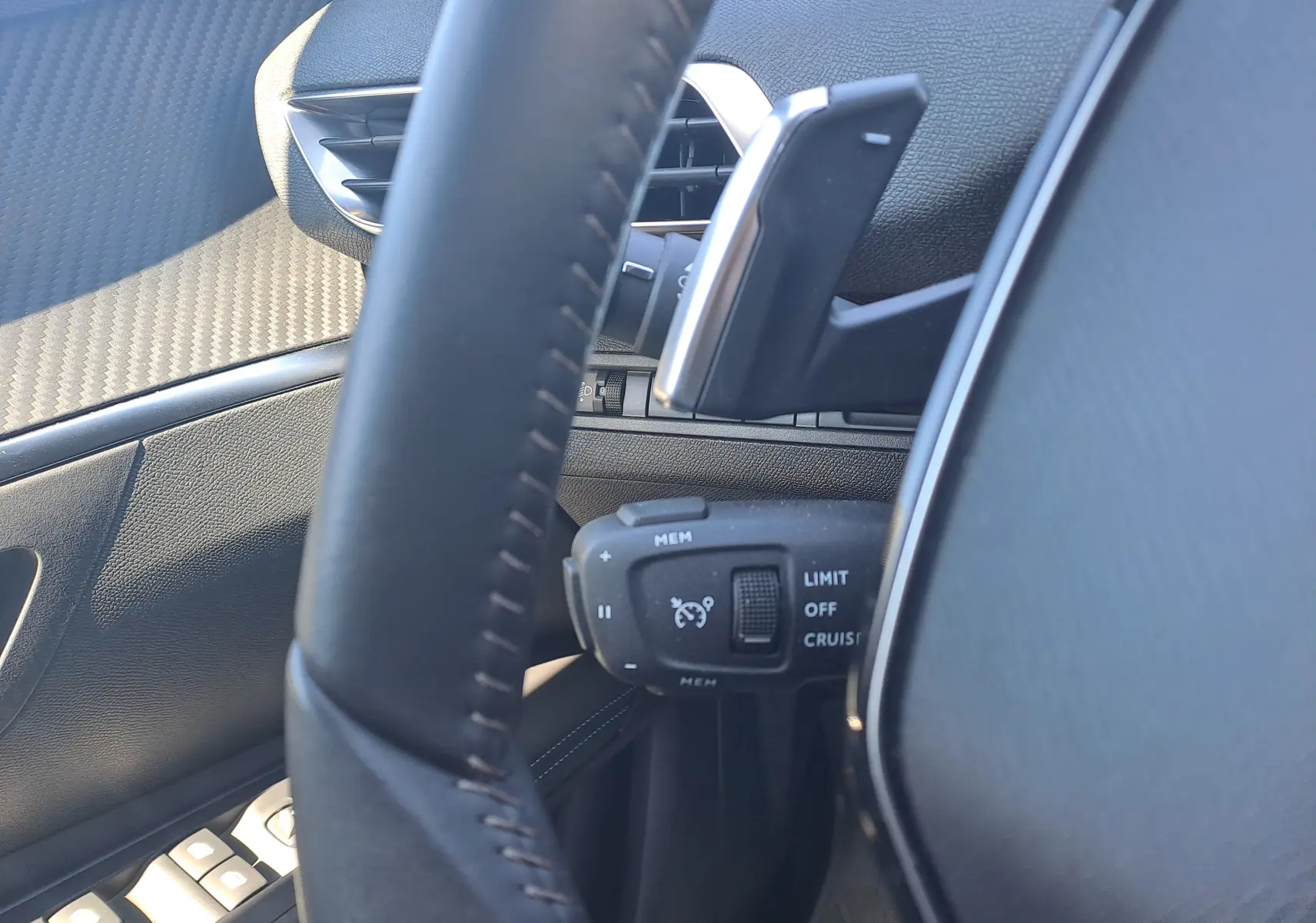 Gros plan sur la commande de régulateur de vitesse derrière le volant noir du Peugeot 3008 2023, intérieur cuir et carbone.