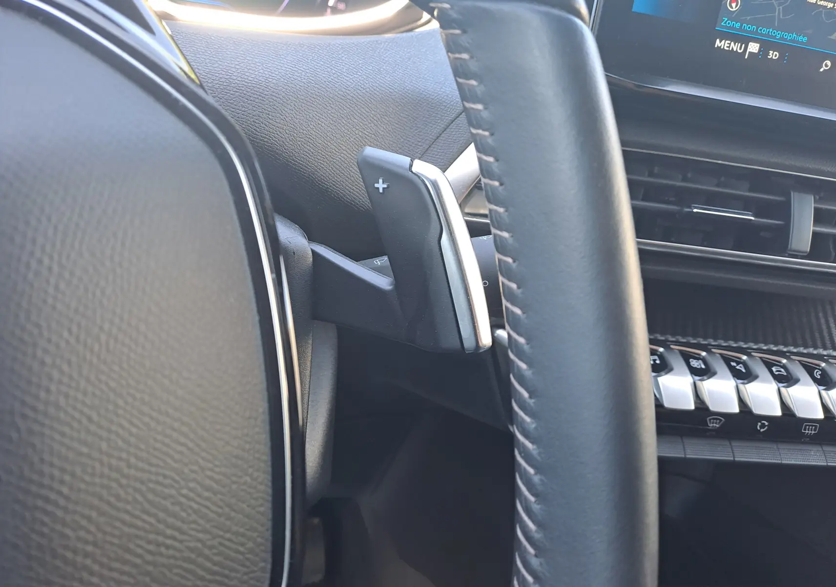 Gros plan sur la palette de changement de vitesse droite du volant cuir noir du Peugeot 3008 2023, avec tableau de bord et écran tactile visibles.