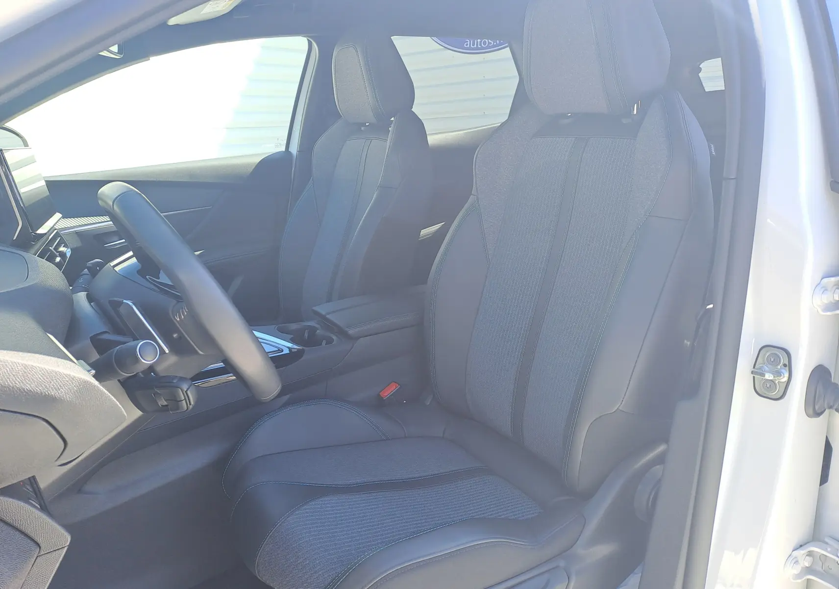 Vue intérieure côté conducteur du Peugeot 3008 2023 blanc nacré, sièges noirs en tissu et cuir avec console centrale visible.
