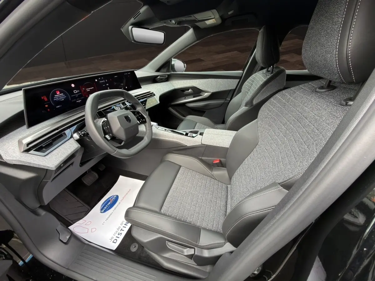 Vue intérieure côté conducteur du Peugeot 3008 noir 2026, sièges tissu et cuir, tableau de bord numérique panoramique.