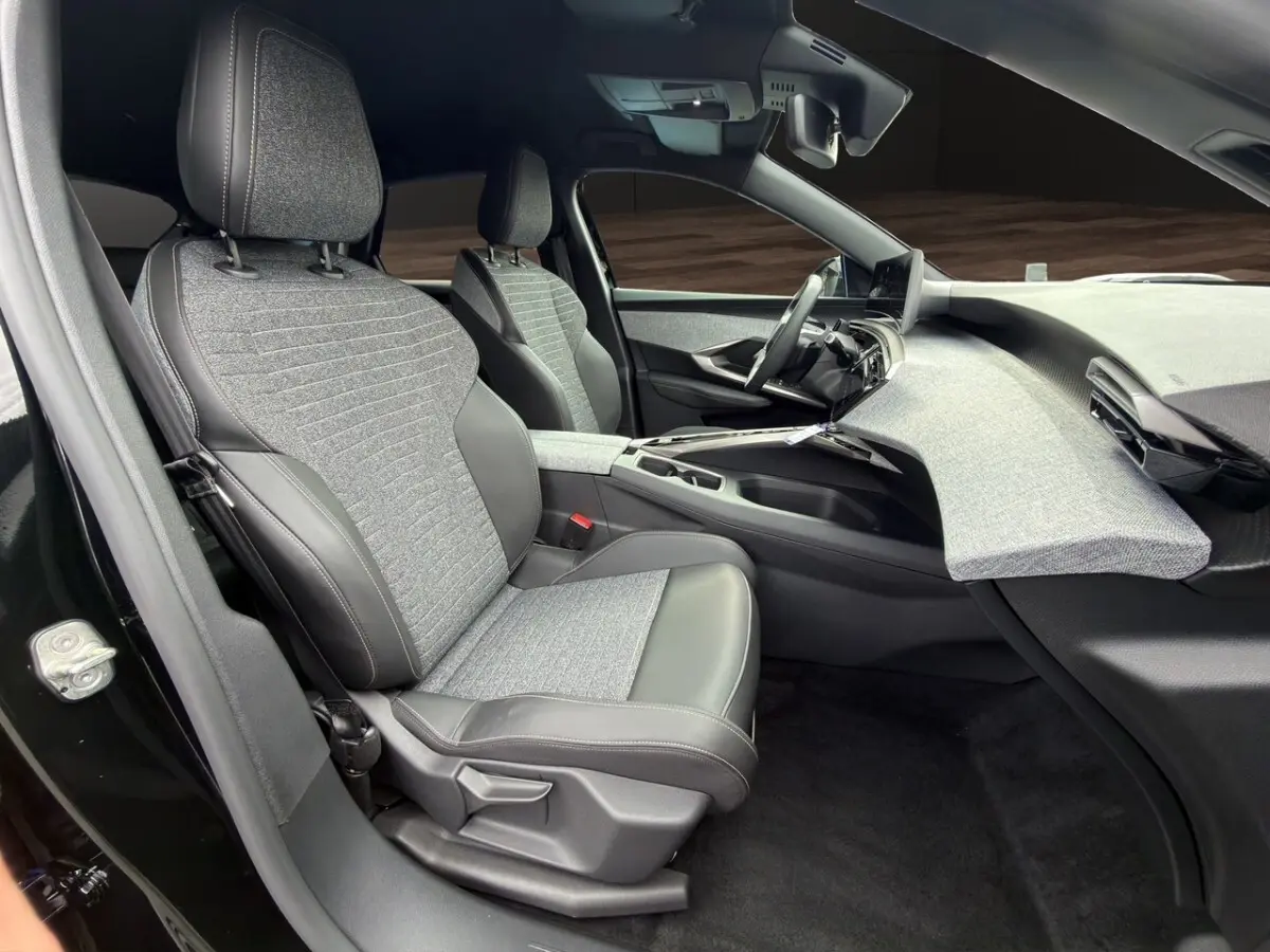 Vue intérieure côté conducteur du Peugeot 3008 noir 2026, sièges tissu et cuir, tableau de bord avec finition tissu gris clair.