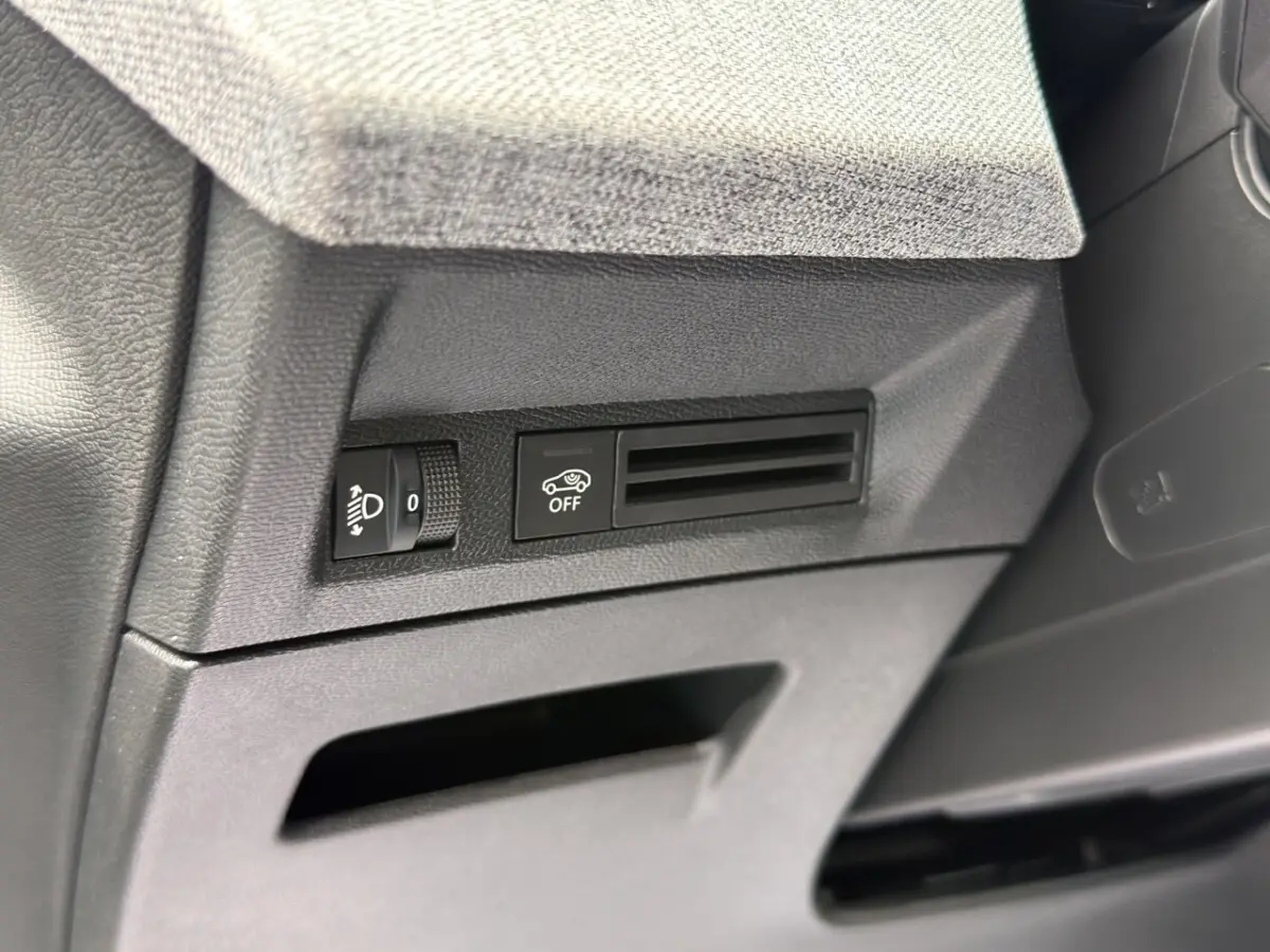 Détail intérieur côté gauche du tableau de bord noir du Peugeot 3008 1.2 Hybrid avec commande réglage phares et bouton off.