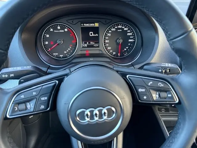 Vue rapprochée du volant cuir noir de l'Audi Q2 35 TFSI 2023 avec tableau de bord digital et compteurs analogiques.