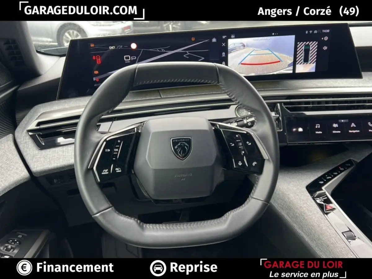 Vue intérieure centrée sur le volant du Peugeot 5008 bleu 2024 avec tableau de bord numérique et caméra de recul affichée.