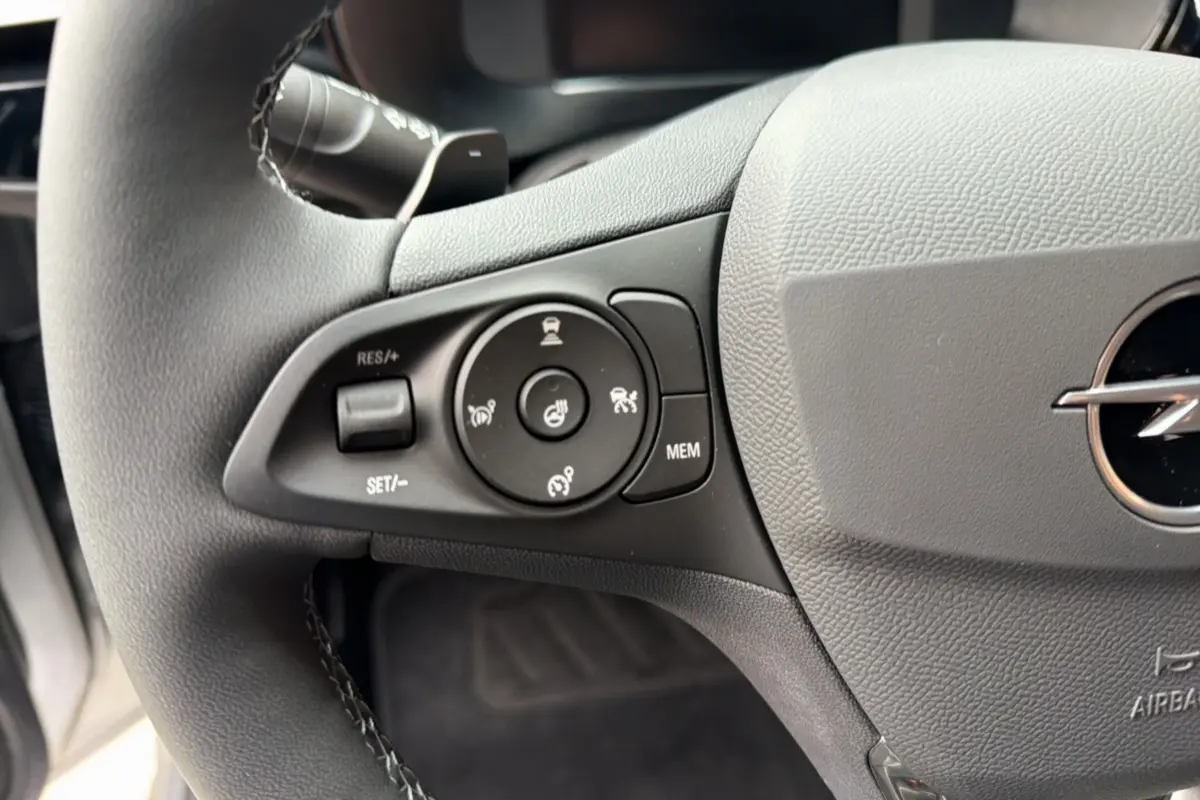 Gros plan sur le volant cuir gris de l’Opel Corsa Hybrid 2026, avec commandes multifonctions et logo Opel visible.