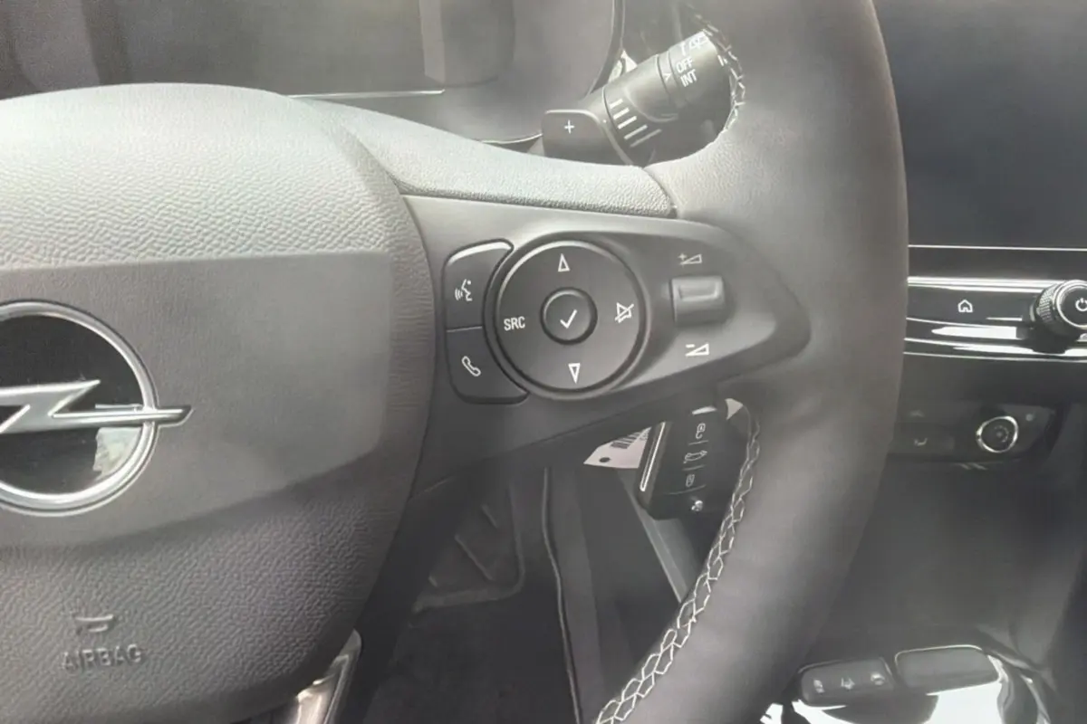 Gros plan sur le volant cuir multifonctions de l’Opel Corsa Hybrid 110 e-DCT6, avec commandes intégrées et logo Opel central.