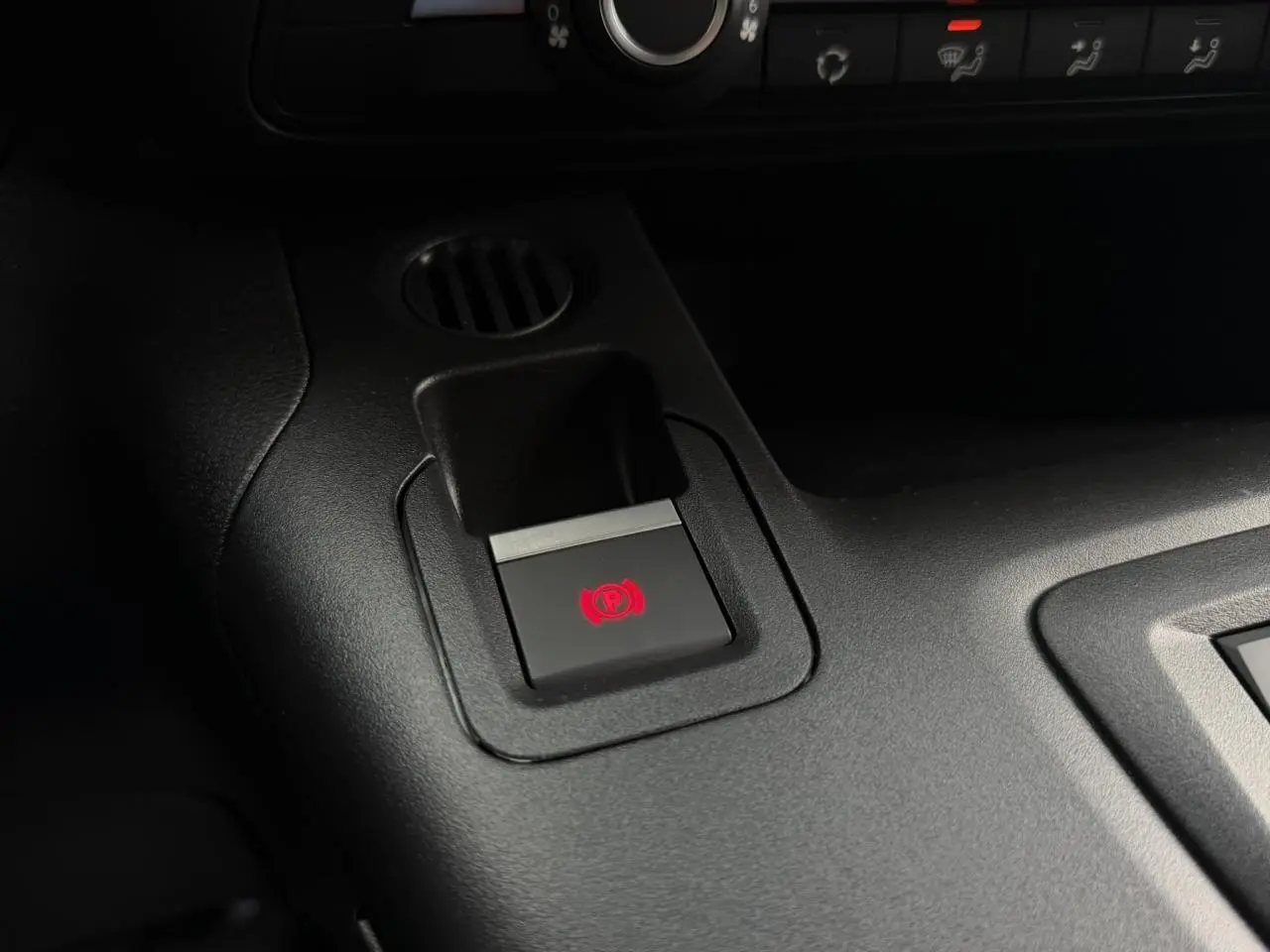 Gros plan sur le bouton de frein de stationnement électrique rouge dans l’habitacle noir du Citroën Berlingo Van XL blanc.